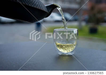 Pouring green tea into a glass from a metal kettle on blurred background, hot drink in teapot 130627565