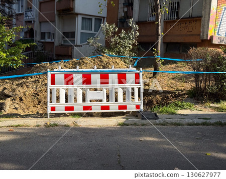 Red and white striped barrier placed in front of soil pile. Construction zone, infrastructure repair and urban maintenance with safety measure and regulation practice. 130627977