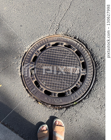Round manhole cover with inscription on asphalt street surface. Infrastructure, engineering, urban service and utility system with industrial design and public environment. Round manhole cover with inscription on asphalt street surface. Infrastructure, engineering, urban service and utility system with industrial design and public environment. 130627998