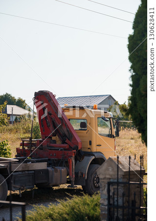 Yellow Crane Truck with Red Arm Parked Beside Roadside Vegetation in Rural Setting, Sunny Day Landscape Photography 130628411