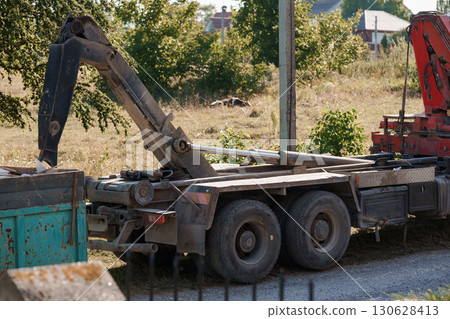 Construction Vehicle with Crane Unloading Materials on Grassy Field, Red and Green Industrial Scene Construction Vehicle with Crane Unloading Materials on Grassy Field, Red and Green Industrial Scene 130628413