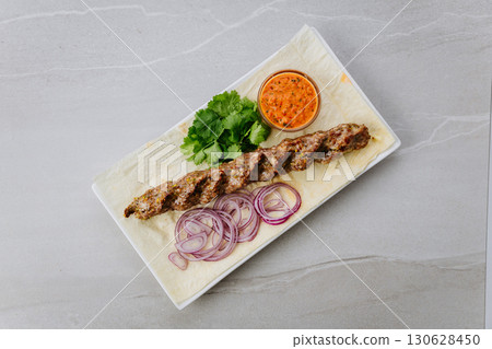 Grilled lamb lula kebab with onion, herbs, and spicy sauce on lavash bread 130628450