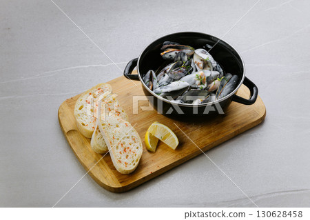 Steamed mussels in creamy sauce served with bread and lemon on wooden board 130628458