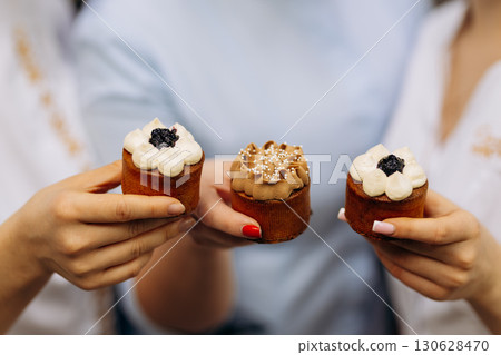 Women holding gourmet mini cakes with whipped cream and chocolate topping in hands 130628470