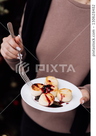 Woman holding plate with cottage cheese pancakes and berry sauce, close-up view 130628482