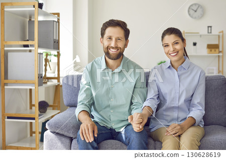 Young happy married couple sitting on the sofa in the living room at home and smiling. Young happy married couple sitting on the sofa in the living room at home and smiling. 130628619