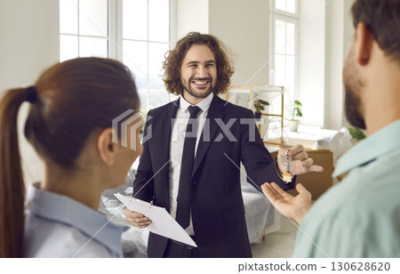 Young male realtor giving house key from new apartments to a happy smiling couple customers. Young male realtor giving house key from new apartments to a happy smiling couple customers. 130628620