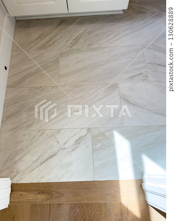 Spacious floor view showing light marble-style tiles paired with a wooden floor edge, under white cabinetry. Useful for real estate or flooring visuals. 130628889