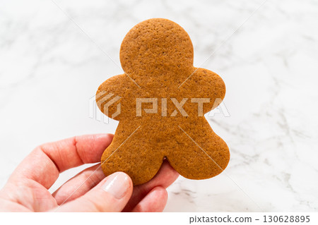 Front view of a hand holding a golden-brown gingerbread man cookie with a plain background. 130628895