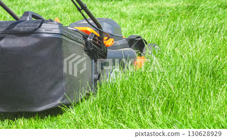 At a residential suburban house, a lush green lawn is meticulously mowed using an electric lawn mower, creating a well-manicured and inviting outdoor space. At a residential suburban house, a lush green lawn is meticulously mowed using an electric lawn mower, creating a well-manicured and inviting outdoor space. 130628929