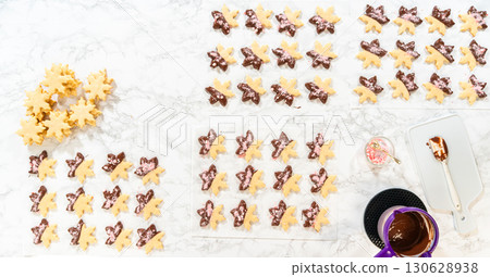 A complete overhead view of decorated snowflake sugar cookies arranged in rows, surrounded by melted chocolate and crushed peppermint, presenting a finished look for the holiday treats. A complete overhead view of decorated snowflake sugar cookies arranged in rows, surrounded by melted chocolate and crushed peppermint, presenting a finished look for the holiday treats. 130628938