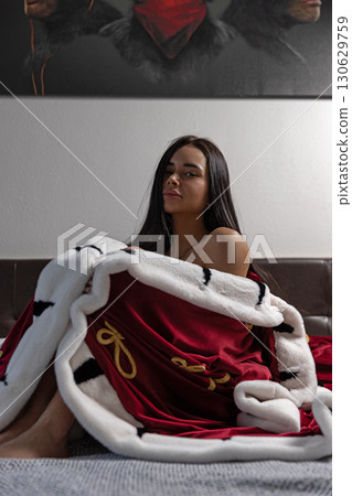 girl wrapped in a luxurious royal robe rests comfortably on a bed her relaxed demeanor adds elegance to the modern bedroom. The soft textures and muted colors create a tranquil ambiance. girl wrapped in a luxurious royal robe rests comfortably on a bed her relaxed demeanor adds elegance to the modern bedroom. The soft textures and muted colors create a tranquil ambiance. 130629759