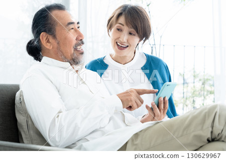 Senior couple looking at smartphone on sofa Senior couple looking at smartphone on sofa 130629967