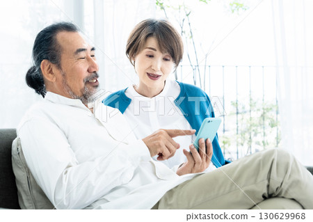 Senior couple looking at smartphone on sofa Senior couple looking at smartphone on sofa 130629968