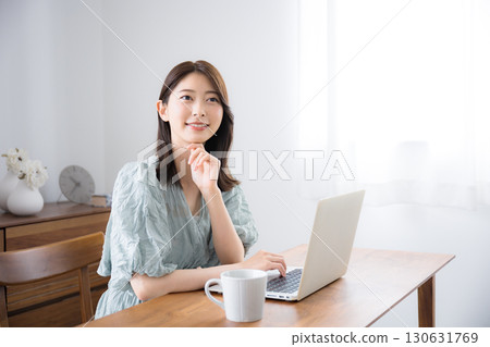 Young pretty woman in casual clothes using laptop in her home room, looking at camera Young pretty woman in casual clothes using laptop in her home room, looking at camera 130631769