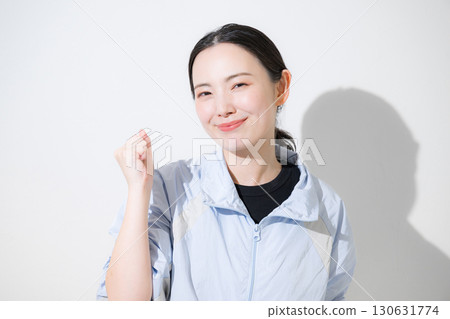 A woman in sportswear cheering with a fist pump, looking at the camera with a smile. I'll do my best with my diet and exercise! 130631774