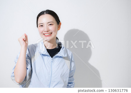 A woman in sportswear cheering with a fist pump, looking at the camera with a smile. I'll do my best with my diet and exercise! 130631776