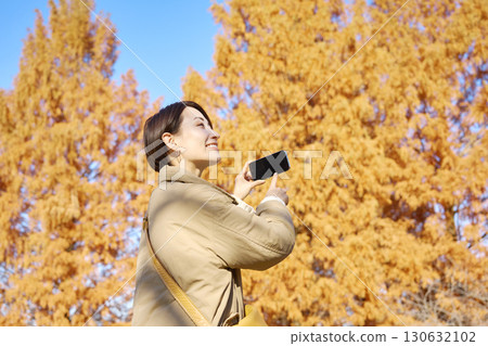 Middle-aged woman taking photos of autumn leaves 130632102