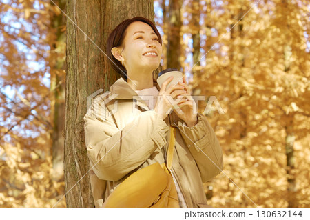 Middle-aged woman drinking coffee among autumn leaves Middle-aged woman drinking coffee among autumn leaves 130632144