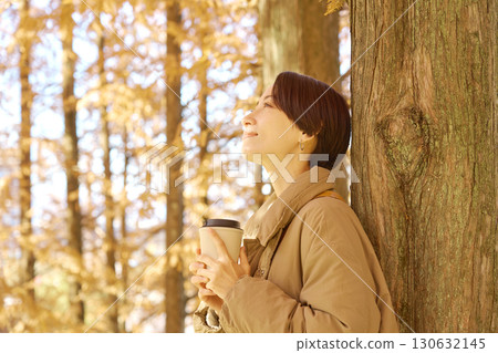 Middle-aged woman drinking coffee among autumn leaves Middle-aged woman drinking coffee among autumn leaves 130632145