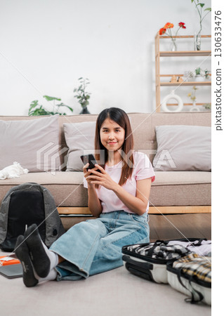 A young woman sits on the floor, packing a suitcase in a bright, modern living room, ready for travel. A young woman sits on the floor, packing a suitcase in a bright, modern living room, ready for travel. 130633476
