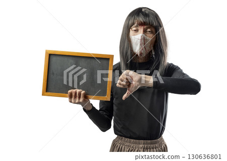 Indonesian southeast asian transgender man dressed as a woman wearing a bloody face mask and holding a blackboard with a thumb down gesture. Copy space. Concept of Halloween, Sister Hong, or red uncle 130636801