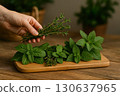 A hand holds a rosemary sprig above a wooden board with various fresh herbs arranged neatly. Generated AI. 130637965
