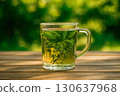 A clear glass mug filled with herbal tea infused with fresh mint and thyme on a wooden table outdoors. Generated AI. 130637968