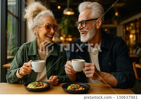 An elderly couple joyfully enjoying coffee and breakfast together in a cozy modern cafe. Generated AI. 130637981