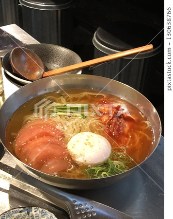 Naengmyeon, a refreshing Korean cold noodle dish served in an icy broth, topped with sliced vegetables, a boiled egg, and spicy sauce. Perfect for summer food photography and Korean cuisine projects. 130638766