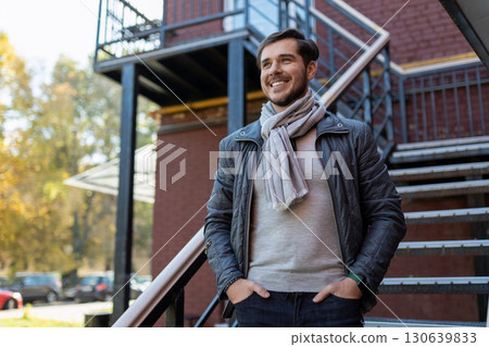 stylish adult man with a wide smile stands and looks at the street 130639833
