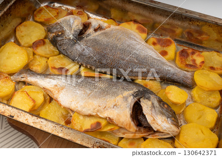 Dorado fish on a baking sheet with potatoes. Whole roasted seabream, gilt-head bream 130642371