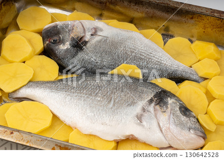 Dorado fish on a baking sheet with potatoes. Whole raw seabream, gilt-head bream, dorada Dorado fish on a baking sheet with potatoes. Whole raw seabream, gilt-head bream, dorada 130642528