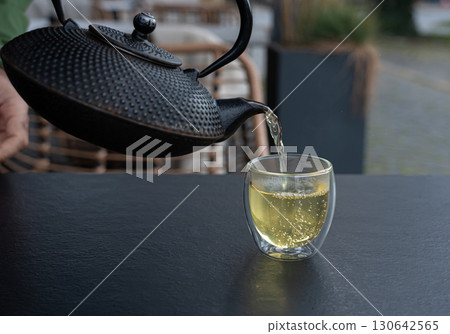 Pouring green tea into a glass from a metal kettle on blurred background, hot drink in teapot Pouring green tea into a glass from a metal kettle on blurred background, hot drink in teapot 130642565