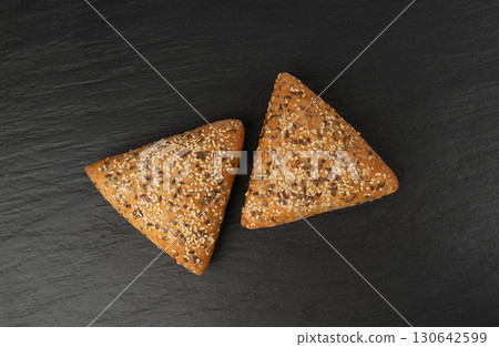 Triangular bun closeup. Wheat bread with sesame and flax seeds, healthy whole grain bakery Triangular bun closeup. Wheat bread with sesame and flax seeds, healthy whole grain bakery 130642599
