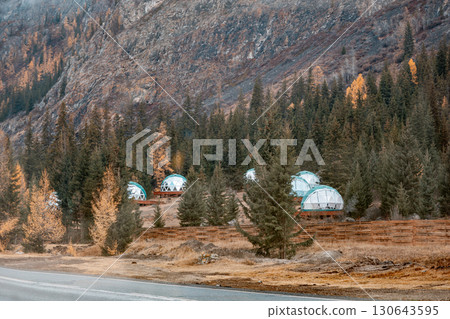 Autumn forest landscape with dome tents for glamping. Quiet place where guests can enjoy wilderness and modern amenities surrounded by fall seasonal colors. Spherical dome house at foot of mountains 130643595