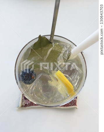A refreshing glass of lemonade with ice cubes, garnished with fresh lemon slices and a sprig of mint, capturing the vibrant yellow color and crisp, citrusy essence. 130643703