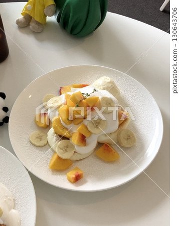 Fluffy souffle pancake topped with airy cream, sweet banana slices, and juicy peaches, offering a perfect blend of soft texture and fruity sweetness in every dreamy, melt-in-your-mouth bite. 130643706