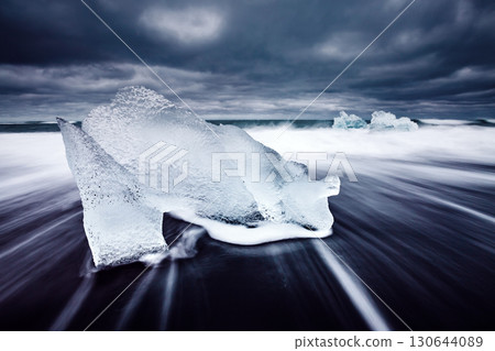 Ice fragments on black sand. Popular tourist attraction. Location Vatnajokull, Jokulsarlon lagoon, Iceland, Europe. Ice fragments on black sand. Popular tourist attraction. Location Vatnajokull, Jokulsarlon lagoon, Iceland, Europe. 130644089