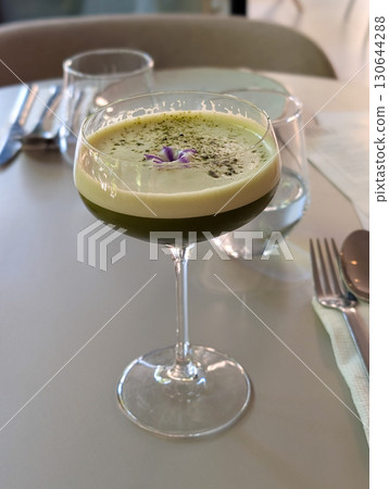 A green cocktail served in a glass with garnish on a cafe table. Culinary art, lifestyle refreshment, and the culture of mixology in a modern dining setting. 130644288