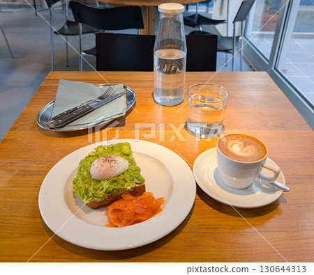 Avocado toast with poached egg and salmon served on a plate in a cafe. Healthy breakfast, fresh ingredients, and gourmet dining. 130644313