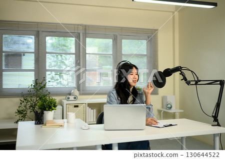 Young woman recording podcast with microphone and laptop in modern home studio Young woman recording podcast with microphone and laptop in modern home studio 130644522