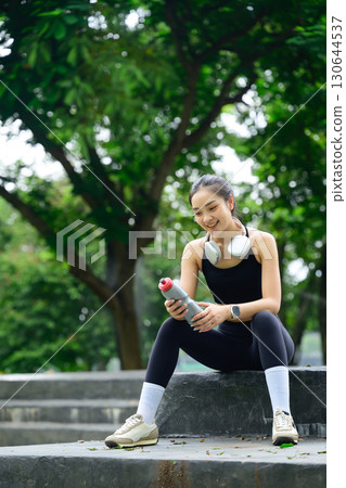Fit female athlete with a water bottle and taking a break after exercise Fit female athlete with a water bottle and taking a break after exercise 130644537