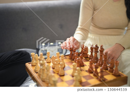Close up of woman moving chess piece on a wooden chessboard during a casual game 130644539