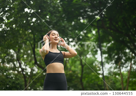 Fit female athlete listening to music in a green park environment Fit female athlete listening to music in a green park environment 130644555