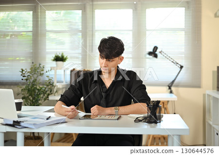 Young businessman working on digital tablet, analyzing charts in modern office 130644576