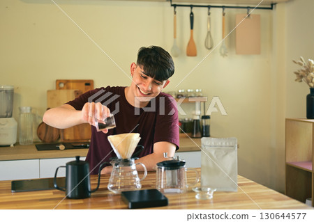 Smiling young man pouring ground coffee into a dripper for manual brewing at home 130644577
