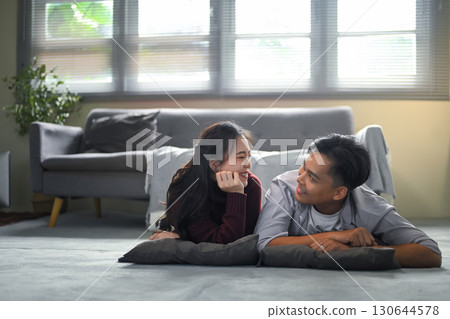 Happy couple lying on the floor with pillows, smiling and looking at each other lovingly at home 130644578