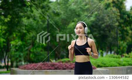 Sporty woman enjoying morning exercise, jogging outdoors with greenery in the background 130644582