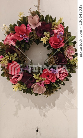 Colorful floral wreath made of artificial flowers hanging on a white wall 130645038